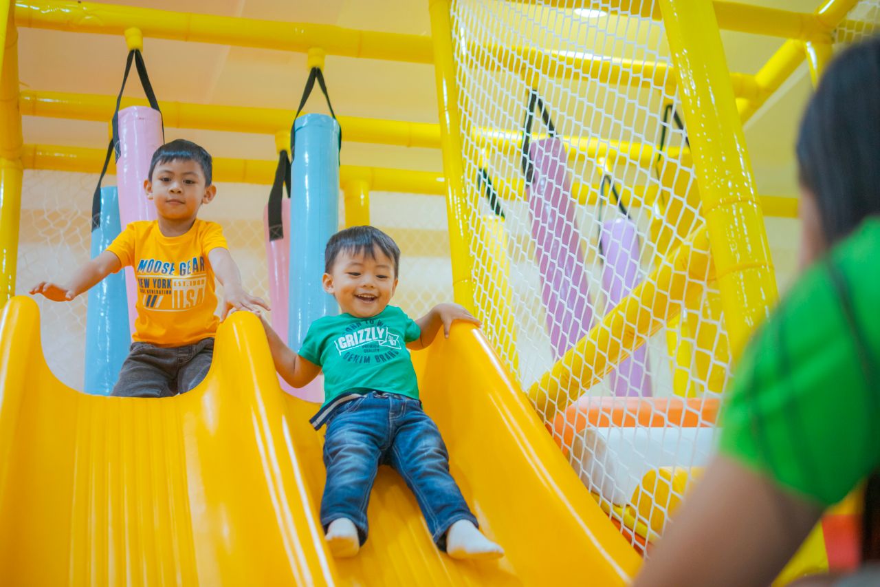 services-03 Two boys enjoying playful moments on a colorful indoor playground slide.