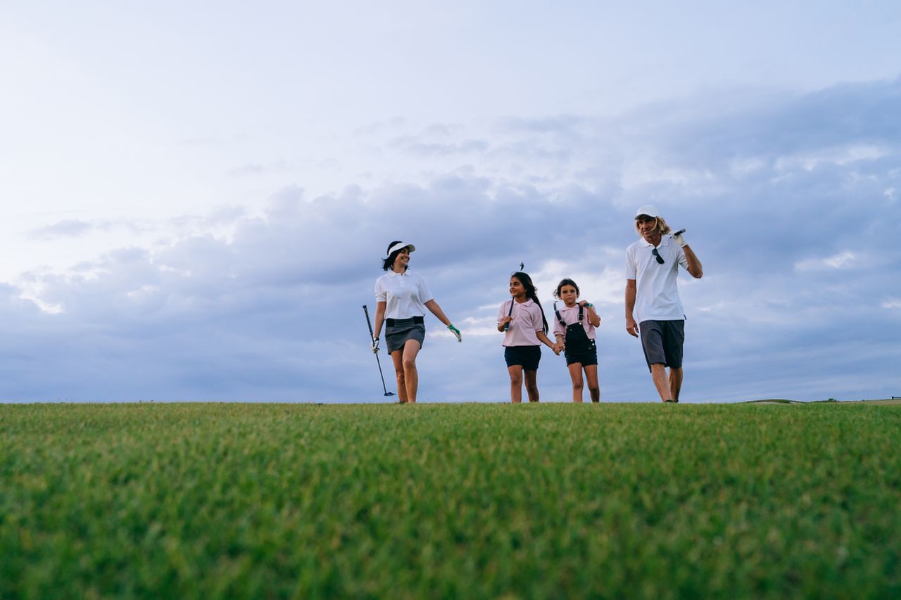 A family of four walking together on a golf course with golf clubs, enjoying the outdoors.