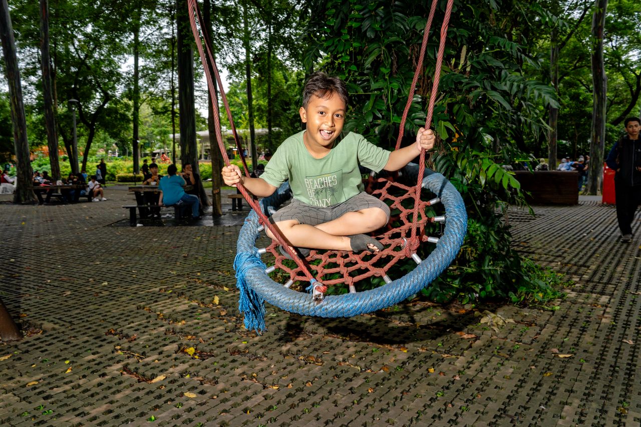 Smiling child on a swing in a vibrant Jakarta park. A joyful outdoor play scene.